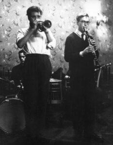 Left to right: Man playing drum kit, man playing trumpet, man playing clarinet