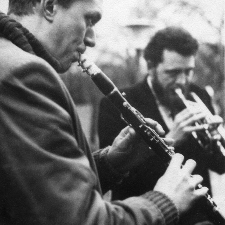 Foreground: Man playing clarinet, Background: Man playing trumpet.